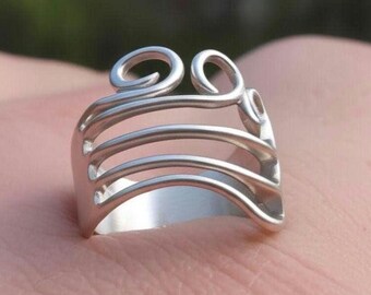 Könnte beinhalten: Ein silberfarbener Ring mit einem einzigartigen Design. Der Ring hat eine Reihe horizontaler Stäbe und dekorative Wirbel oben. Der Ring besteht aus glänzendem Metall und hat eine glatte Oberfläche.