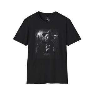 May include: Black t-shirt featuring a grayscale image of a person in a witch hat and cape, holding a staff with a skull. The image includes the text "I was the victim m'lord."