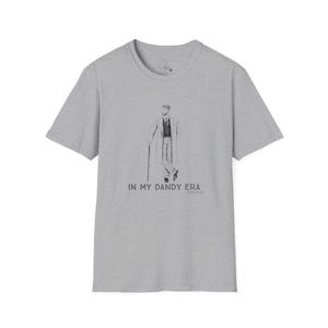 May include: A heather gray t-shirt featuring a graphic of a man with a cane, dressed in a suit. The text "IN MY DANDY ERA" is printed below the illustration. The shirt has short sleeves and a crew neck.
