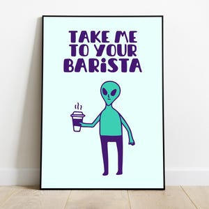 Op de afbeelding: Een ingelijste kunstprint met een cartoon alien die een koffiekopje vasthoudt. De alien is zeegroen met paarse benen en de tekst "TAKE ME TO YOUR BARISTA" in paars erboven. De achtergrond is lichtblauw.
