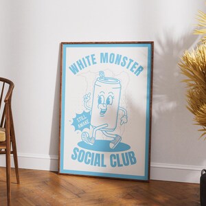 May include: A framed poster with a cartoon illustration of a smiling soda can character in light blue on a white background. The poster reads "WHITE MONSTER SOCIAL CLUB" with the words "STILL AWAKE" on a speech bubble.