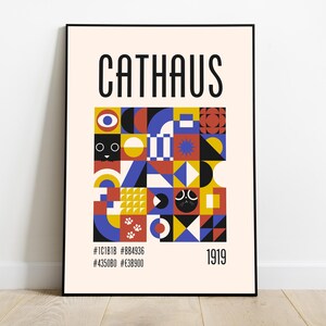 Op de afbeelding: Een ingelijste kunstdruk met het woord "CATHAUS" in zwart boven een kleurrijk geometrisch ontwerp. Het ontwerp bevat vierkanten en vormen in rood, blauw, geel en zwart, met katachtige gezichten. Het jaar "1919" staat onderaan.
