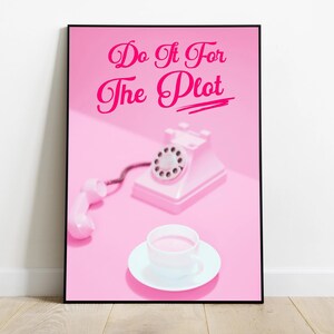 May include: A pink poster with the text "Do It For The Plot" in pink cursive lettering. A pink rotary phone and a white cup of coffee are on a pink surface.
