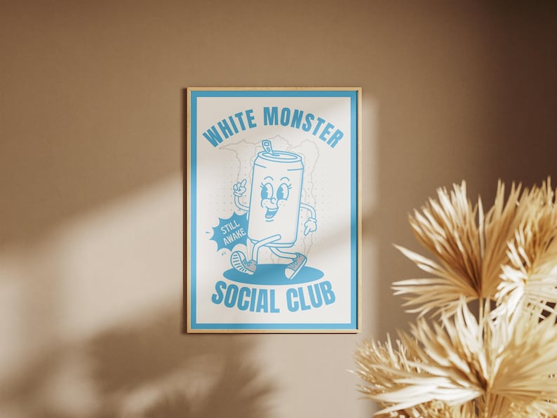 May include: A framed poster with a light blue cartoon design on a white background. The design features a walking soda can character with the text "WHITE MONSTER SOCIAL CLUB" and "STILL AWAKE". The frame is a light wood color.