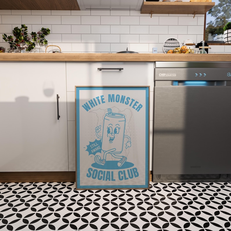 May include: A framed poster with a light blue border and the words "WHITE MONSTER SOCIAL CLUB" in a retro font. The poster features a cartoon can character with a smiling face and the words "STILL AWAKE". The poster is displayed in a kitchen.