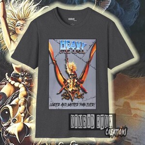 May include: Dark gray t-shirt featuring a graphic with the words "Heavy Metal" in a blue and silver design. The graphic shows a winged creature with a female figure. The text "Louder and Nastier Than Ever!" is below the graphic.