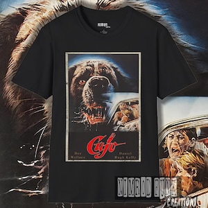 May include: Black t-shirt with a vintage movie poster print of the horror film "Cujo". The poster features a close-up of a snarling dog's face and the text "Cujo", "Dee Wallace", and "Daniel Hugh Kelly".