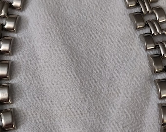 May include: A silver-toned metal necklace featuring a series of interlocking, rectangular links arranged in a double-row pattern. The links have a smooth, polished finish and are connected to form a continuous, flexible chain structure.