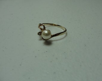 May include: A gold-toned ring featuring a large, round, white pearl as the focal point. A small, clear gemstone accents the pearl. The ring has a delicate, flowing design, suitable for a special occasion.