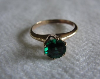 May include: A gold ring with a large, round, dark green gemstone.