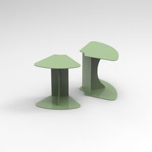 Può includere: Due tavolini moderni verde chiaro. Uno ha un piano triangolare e una base rettangolare. L'altro ha un piano curvo e una base curva. Entrambi i tavoli sono realizzati in materiale solido e hanno un design minimalista.