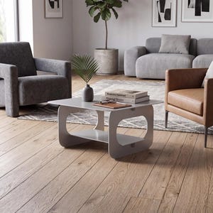 May include: A light gray coffee table with a rectangular top and a lower shelf, featuring rounded cutouts on the side supports. The table holds a small gray vase with a green plant, a brown notebook, and two books titled Modernism Redefined and Material Stories.