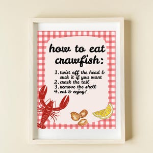 K&ouml;nnte beinhalten: Ein roter und wei&szlig;er karierter Hintergrund mit einem wei&szlig;en Rahmen. Der Text "how to eat crawfish:" ist in Schwarz geschrieben. Der Text unter dem Titel lautet "1. twist off the head & suck it if you want 2. crack the tail 3. remove the shell 4. eat & enjoy!" Es gibt eine Illustration eines roten Krebses und eine Zeichnung von Krebs-Schw&auml;nzen und einer Zitronenscheibe.