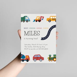 Könnte beinhalten: Eine weiße Einladungskarte mit einem blauen, schwarzen und weißen Straßen-Design. Die Karte trägt den Text "Beep. Zoom. Honk. Choo. Miles wird zwei!" und Details für eine Geburtstagsfeier. Die Karte ist mit bunten Illustrationen von Spielzeugfahrzeugen verziert, darunter ein LKW, ein Bulldozer, ein Schulbus, ein Betonmischer, ein Auto und ein Zug.