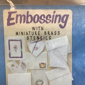 May include: A craft kit for embossing with miniature brass stencils. The kit includes various paper samples with embossed designs, including floral and heart motifs. The text "Embossing with Miniature Brass Stencils" is visible.