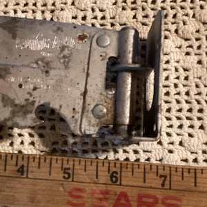 May include: Close-up of a vintage metal can opener with a wooden ruler. The can opener is silver with some rust spots. The ruler is wooden with the word "SEARS" printed in red.