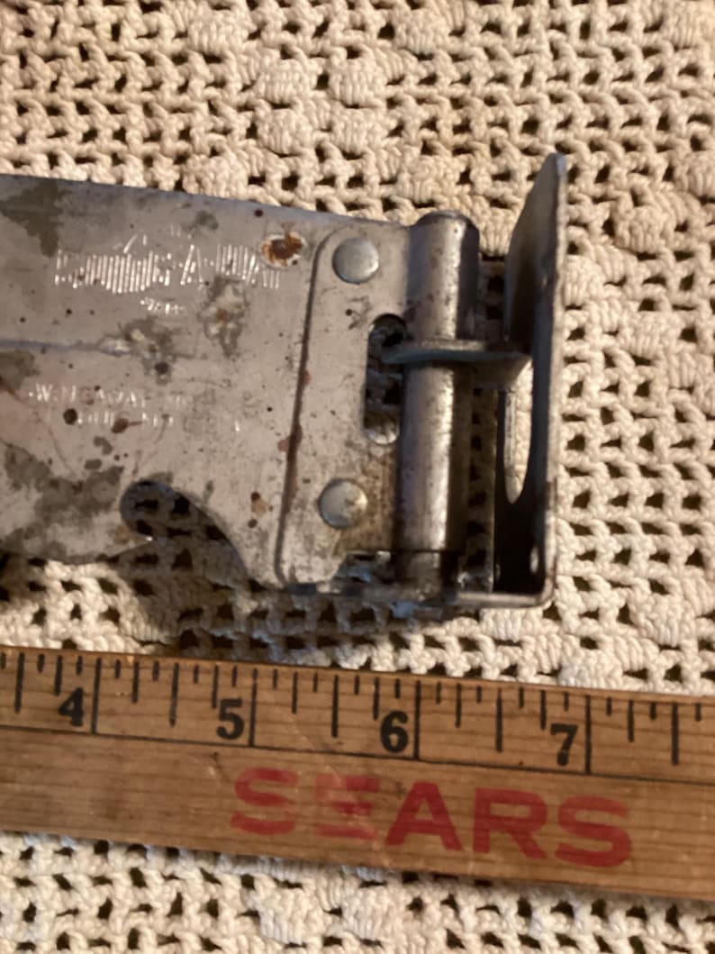 May include: Close-up of a vintage metal can opener with a wooden ruler. The can opener is silver with some rust spots. The ruler is wooden with the word "SEARS" printed in red.