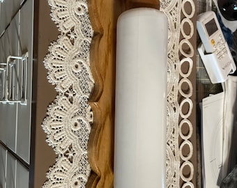 May include: A vintage wall-mounted light fixture with a white cylindrical shade and a wooden frame. The frame has a decorative, scalloped edge and is made of light-colored wood. The fixture is designed to be mounted on a wall.