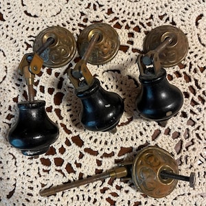 May include: Five antique cabinet knobs with black wooden bases and ornate brass tops. The knobs have a decorative floral design and are attached to a screw.