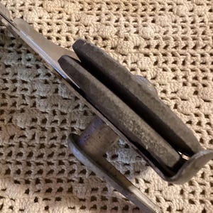 May include: Close-up of a vintage metal tool with a red handle. The tool has a silver blade and a gray, rectangular grip. The tool is designed for a specific purpose, likely related to cutting or shaping materials.