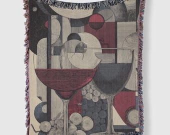 May include: Throw blanket with a wine-themed design. The artwork features two wine glasses, grapes, and geometric shapes in shades of red, gray, and beige. The blanket has a fringed edge.