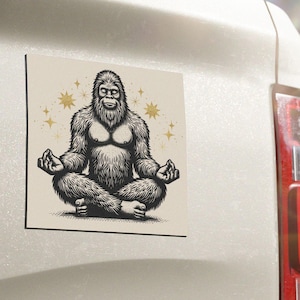 May include: A black and white illustration of a meditating Bigfoot with a beige background and gold stars. The Bigfoot is sitting in a lotus position with its hands in a mudra.