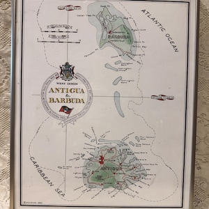 May include: A framed map of Antigua and Barbuda featuring detailed coastlines, geographical landmarks, and the national flag. The map includes text labels for various bays, points, and towns, with the Atlantic Ocean and Caribbean Sea labeled.
