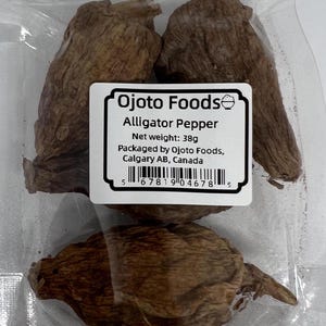 Peut inclure: Un sachet de poivre d'alligator séché, une épice utilisée dans la cuisine ouest-africaine. Le sachet est étiqueté "Ojoto Foods Alligator Pepper" et a un poids net de 38 grammes. Le sachet est également étiqueté avec le nom et l'emplacement de l'entreprise : "Emballé par Ojoto Foods, Calgary AB, Canada".