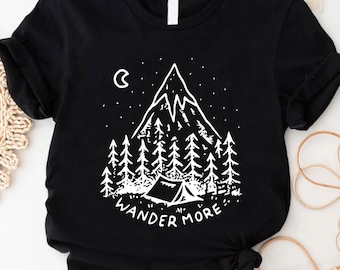 May include: Black t-shirt with a white graphic of a mountain, trees, a tent, and a crescent moon. The text "WANDER MORE" is printed below the graphic. The shirt is made of a soft material and has short sleeves.