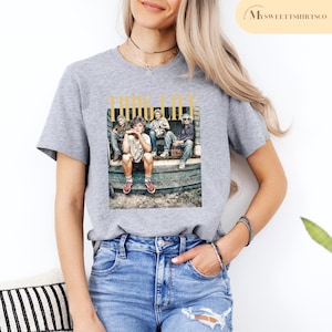May include: Gray t-shirt with a graphic print of four people sitting on a porch. The graphic includes the text "THUG LIFE".