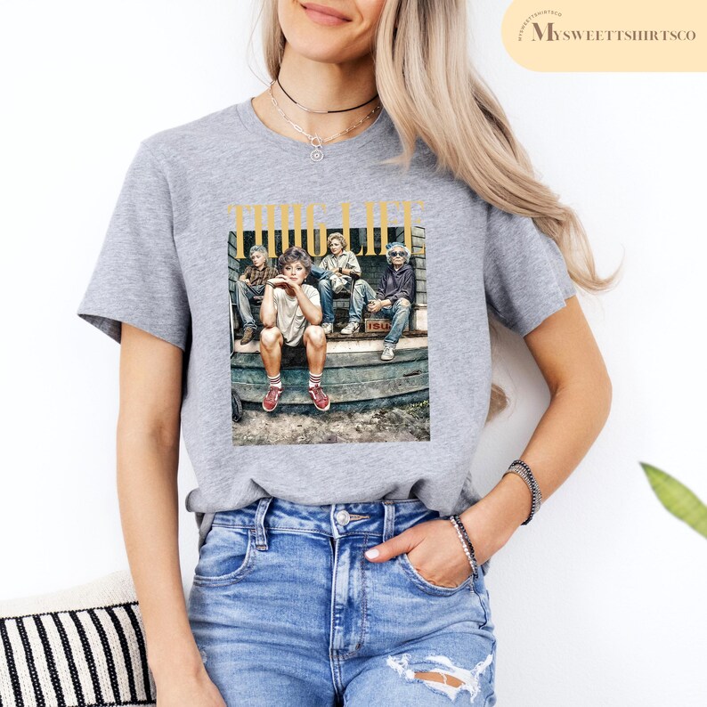 May include: Gray t-shirt with a graphic print of four people sitting on a porch. The graphic includes the text "THUG LIFE".