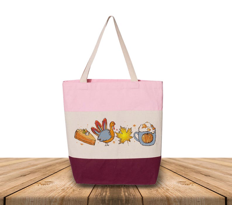 May include: A pink, cream, and burgundy tote bag with cream-colored handles. The bag features a colorful illustration of a slice of pie, a turkey, a maple leaf, and a pumpkin spice latte. The bag is made of canvas.