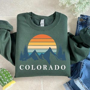 a green shirt with the word colorado on it next to a cactus