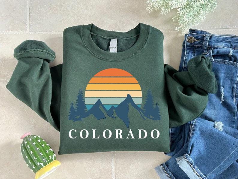 a green shirt with the word colorado on it next to a cactus
