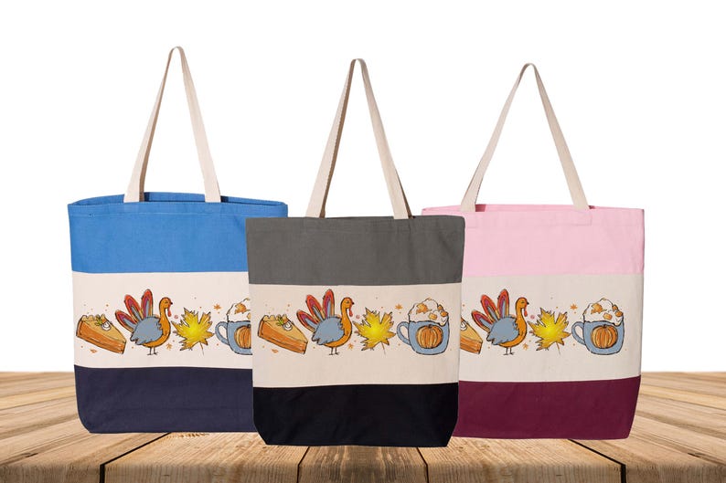 May include: Three canvas tote bags in blue, gray, and pink, each with a cream-colored top and bottom. A Thanksgiving-themed design is printed on a cream band, featuring a turkey, pumpkin spice latte, and pie.