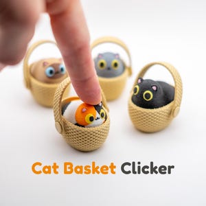 May include: Four small cat basket clickers featuring miniature cats in tan woven-style baskets. The cats are calico, black, gray, and tan with large yellow or blue eyes. The text Cat Basket Clicker is printed in orange and gray below the items.