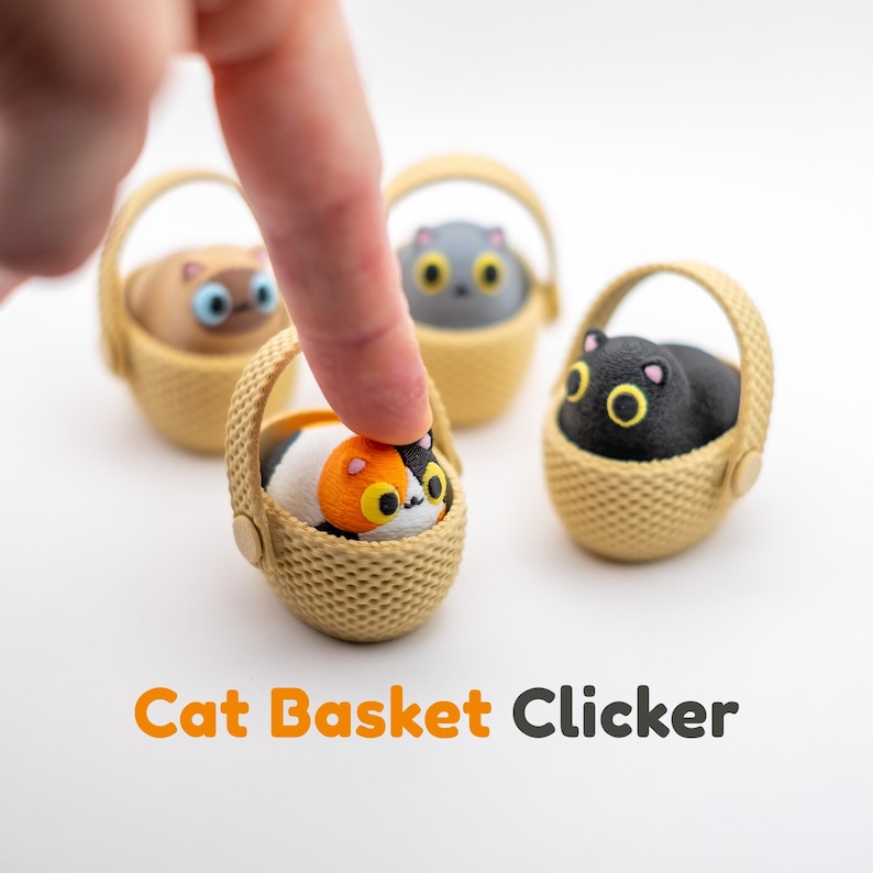 May include: Four small cat basket clickers featuring miniature cats in tan woven-style baskets. The cats are calico, black, gray, and tan with large yellow or blue eyes. The text Cat Basket Clicker is printed in orange and gray below the items.