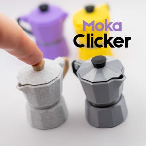 May include: A collection of colorful miniature coffee makers, including gray, purple, and yellow. The text "Moka Clicker" is displayed in purple and black. One finger is touching the top of a gray coffee maker.