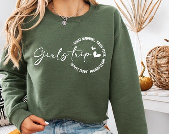 May include: A green sweatshirt with the text "Girls Trip" in white cursive lettering. The text is surrounded by a circle of smaller white text that reads "Great Memories, Great Times, Great Friends, Great Laughs, Sunshine, Girls Trip".