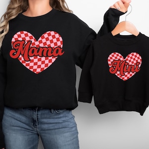 May include: Matching black sweatshirts with a red and pink checkered heart design. The adult sweatshirt says "Mama" and the child's sweatshirt says "Mini".