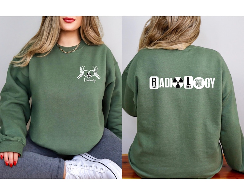 May include: Green sweatshirt with a white graphic of two skeleton hands holding a heart with the word "Radiology" written below. The back of the sweatshirt has the word "RADIOLOGY" written in white with a black radiation symbol and a black and white image of a rib cage.