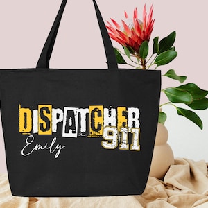 May include: Black tote bag with the text "Dispatcher 911" in yellow and white letters. The name "Emily" is written in white below the text.