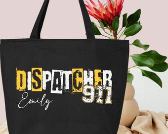 May include: Black tote bag with the text "Dispatcher 911" in yellow and white letters. The name "Emily" is written in white below the text.
