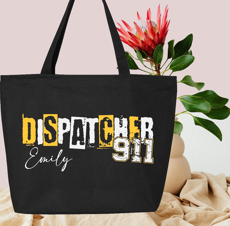 May include: Black tote bag with the text "Dispatcher 911" in yellow and white letters. The name "Emily" is written in white below the text.