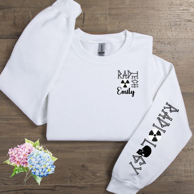 May include: White sweatshirt with black text that reads "Rad Tech Emily" and a radiation symbol on the front. The left sleeve has black text that reads "Radiology" with a radiation symbol and bones.
