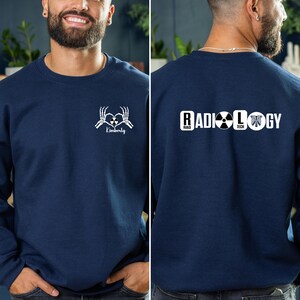 May include: A navy blue sweatshirt with a white skeleton hand design on the front that says "Kimberly" and a white design on the back that says "RADIOLOGY" with a radiation symbol and a ribcage graphic.