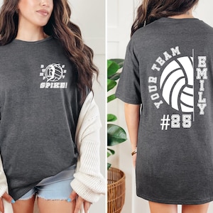 May include: A dark grey t-shirt with a volleyball graphic and the text "Spike!" on the front. The back of the shirt has a volleyball graphic with the text "Your Team" and "Emily #25".