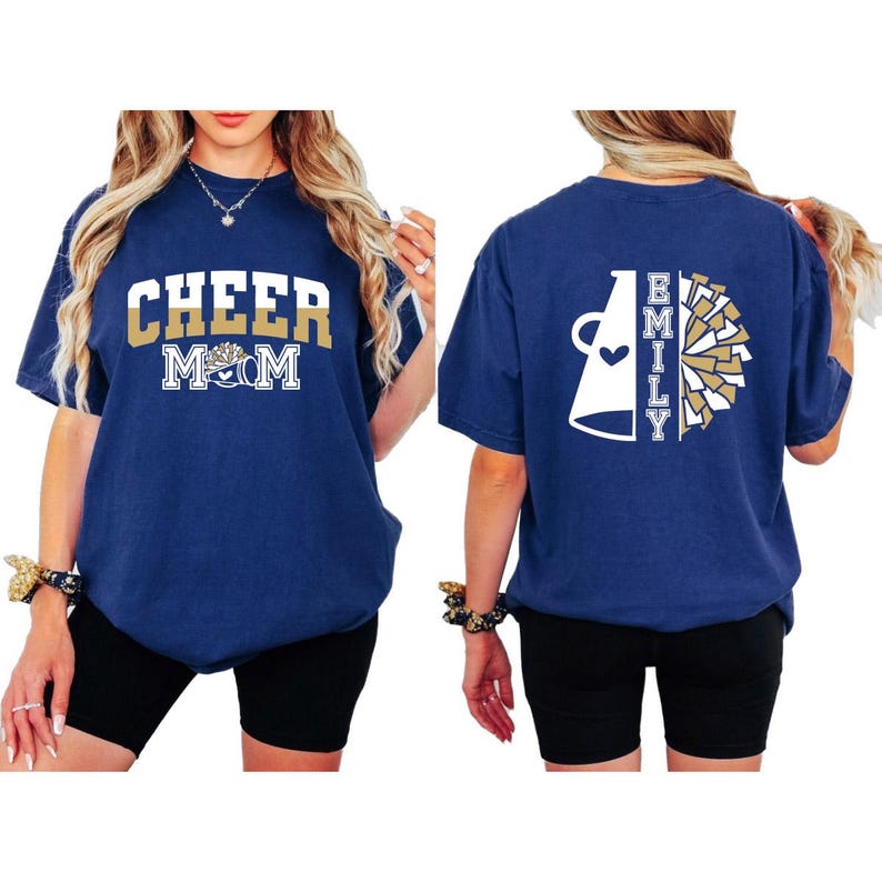 Pu&ograve; includere: Maglietta blu navy con il testo "Cheer Mom" e una grafica di cheerleader dorata e bianca sul davanti. La parte posteriore della maglietta ha un megafono bianco con un cuore e il testo "Emily" in oro e bianco.