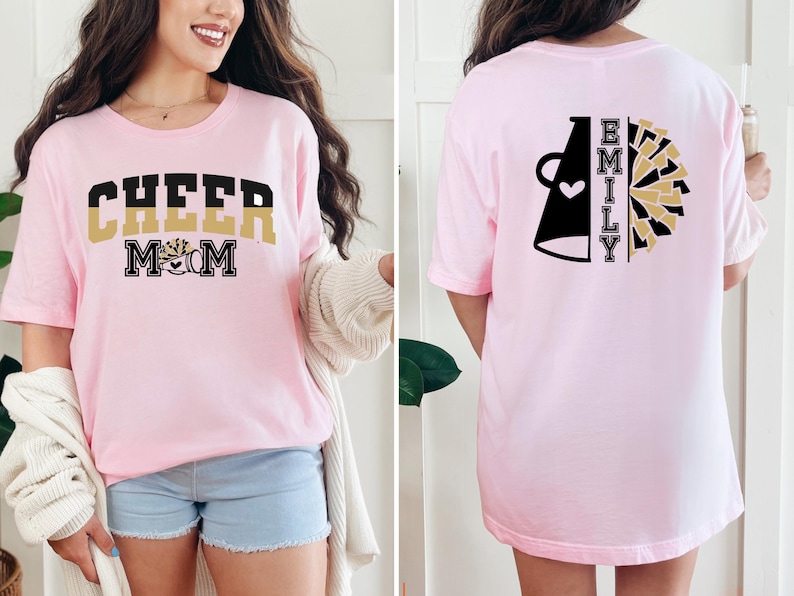 Pu&ograve; includere: Maglietta rosa con il testo "CHEER MOM" in nero e oro sul davanti e un megafono nero con un cuore e il testo "EMILY" in oro sul retro.