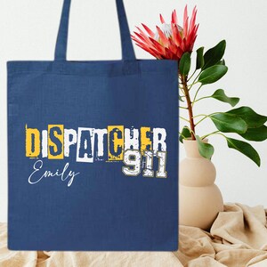 May include: A blue canvas tote bag with the text "Dispatcher 911" in yellow and white letters. The name "Emily" is written in white below the text.